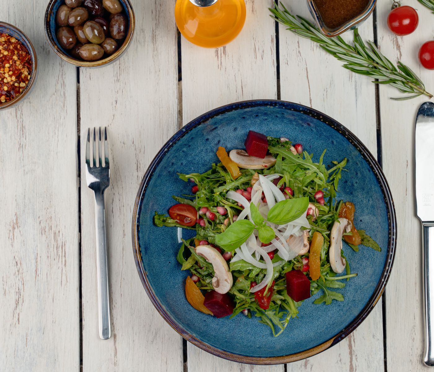 Salade de roquette, champignons et grenade dans une assiette bleue, sur une table en bois clair
